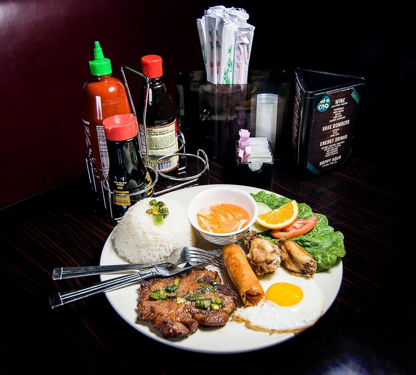 Vietnamese combo plate with grilled pork, rice, fried egg, spring roll, chicken wings, and salad.