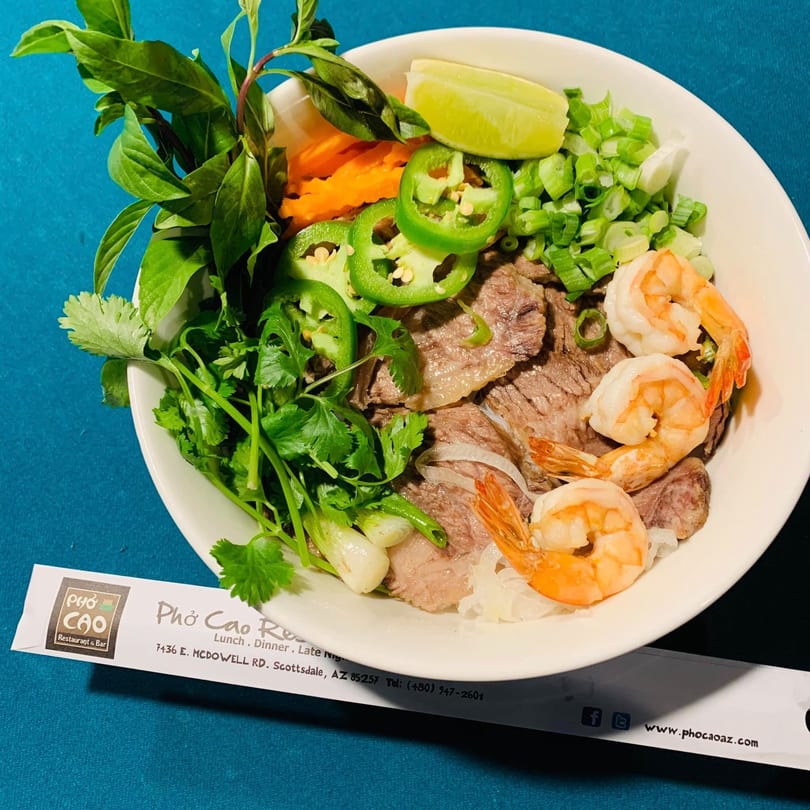 A bowl of Pho Cao pho with beef, shrimp, jalapeños, lime, carrots, and fresh herbs.